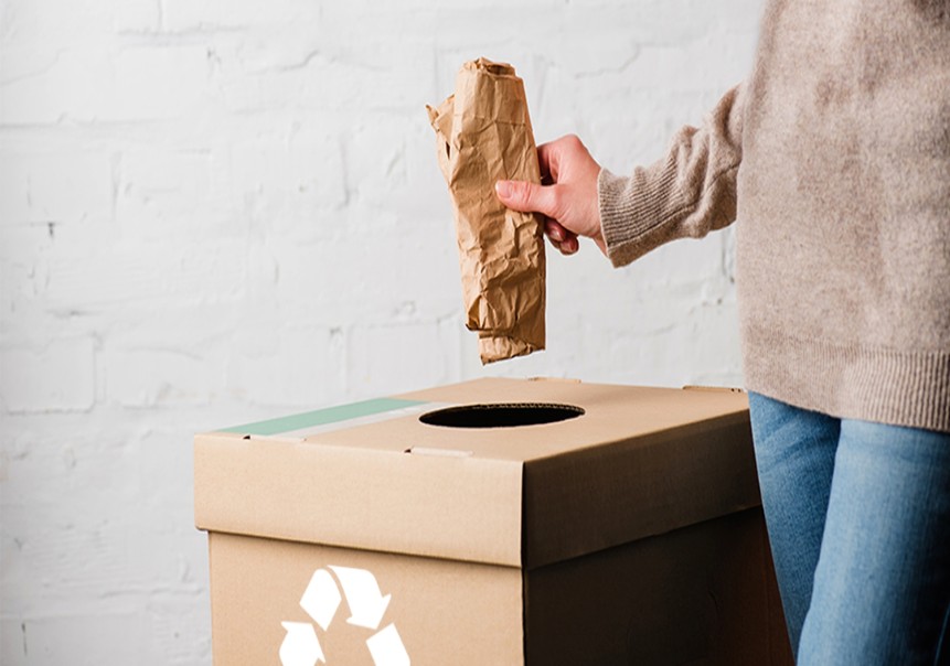 Persona colocando papel kraft en un contenedor de reciclaje de cartón 